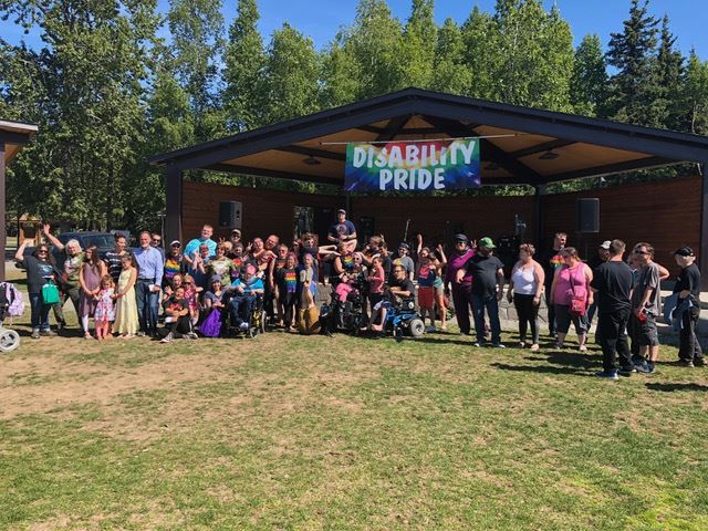 Image of a group of people in a park under a Banneer that says Disability Pride